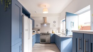 A modern kitchen with blue cabinets, a stainless steel stove, and a white countertop. - Lan y Môr : Family-Friendly 3‑Bed Cottage with Beach Access in Rhosneigr | Managed by Anglesey Holid (Rhosneigr)