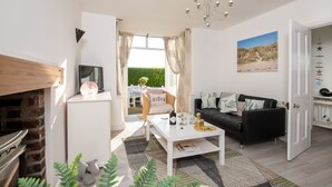 A living room with a fireplace, a television, a coffee table, a sofa, and a dining area with a table and chairs. - Lan y Môr : Family-Friendly 3‑Bed Cottage with Beach Access in Rhosneigr | Managed by Anglesey Holid (Rhosneigr)