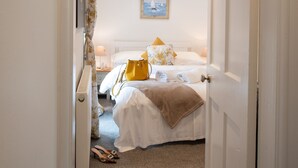 A hotel room with two beds, a painting on the wall, and a yellow bag on one bed. - Lan y Môr : Family-Friendly 3‑Bed Cottage with Beach Access in Rhosneigr | Managed by Anglesey Holid (Rhosneigr)