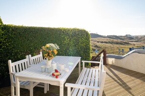 A white wooden table with chairs, a vase of flowers, and a plate with strawberries and a cake.