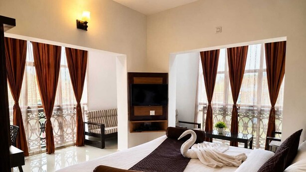 A hotel room with a bed, a TV, a balcony with curtains, and a sofa. - Hotel Al Wesal International (Madikeri)