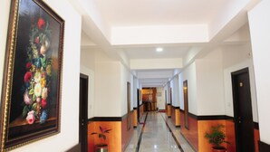 A hotel corridor with a large floral painting on the left, a polished floor, and doors on both sides. - Hotel Al Wesal International (Madikeri)
