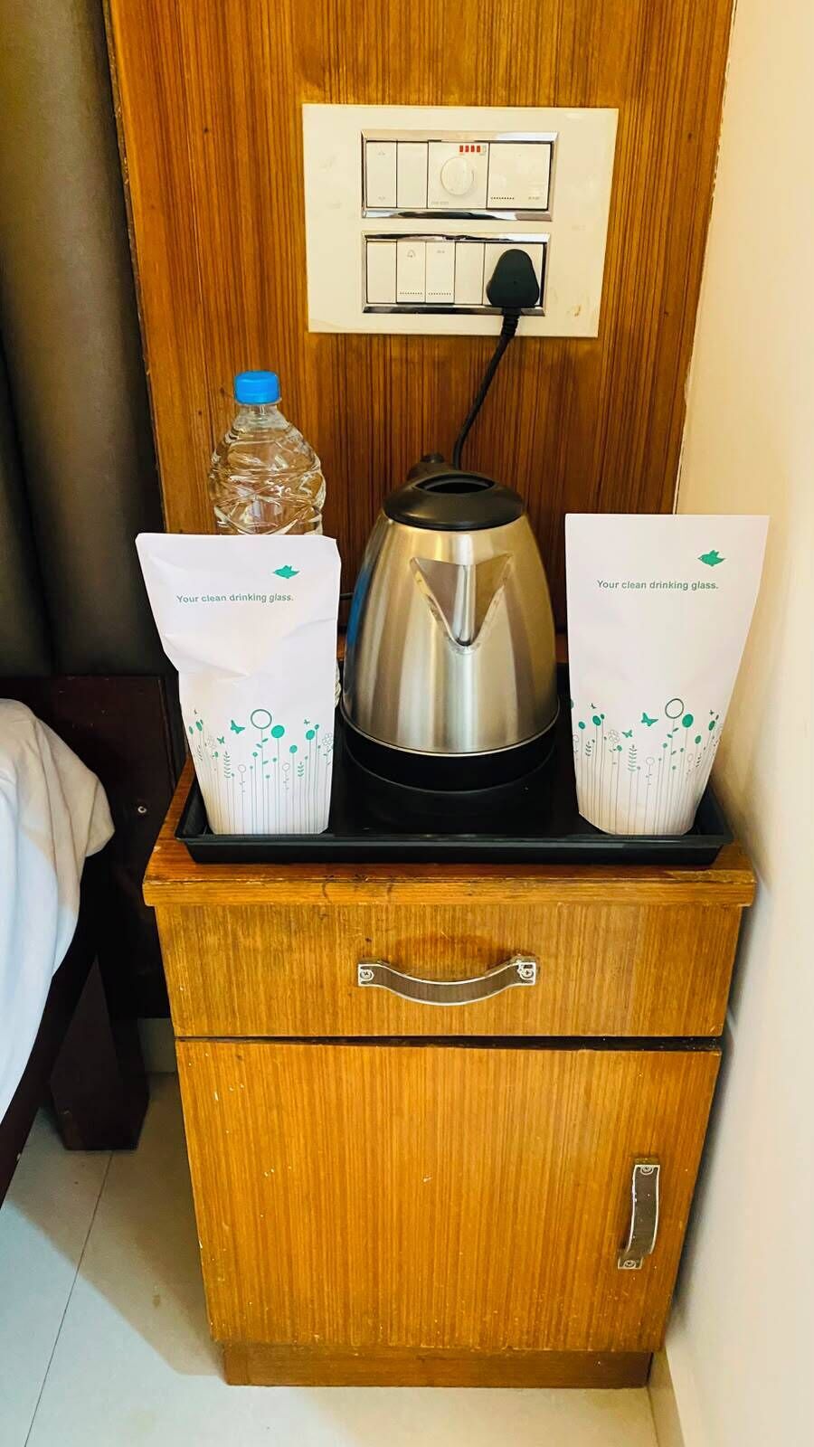 A compact kitchenette with a kettle, a bottle of water, and two bags of clean drinking glasses.