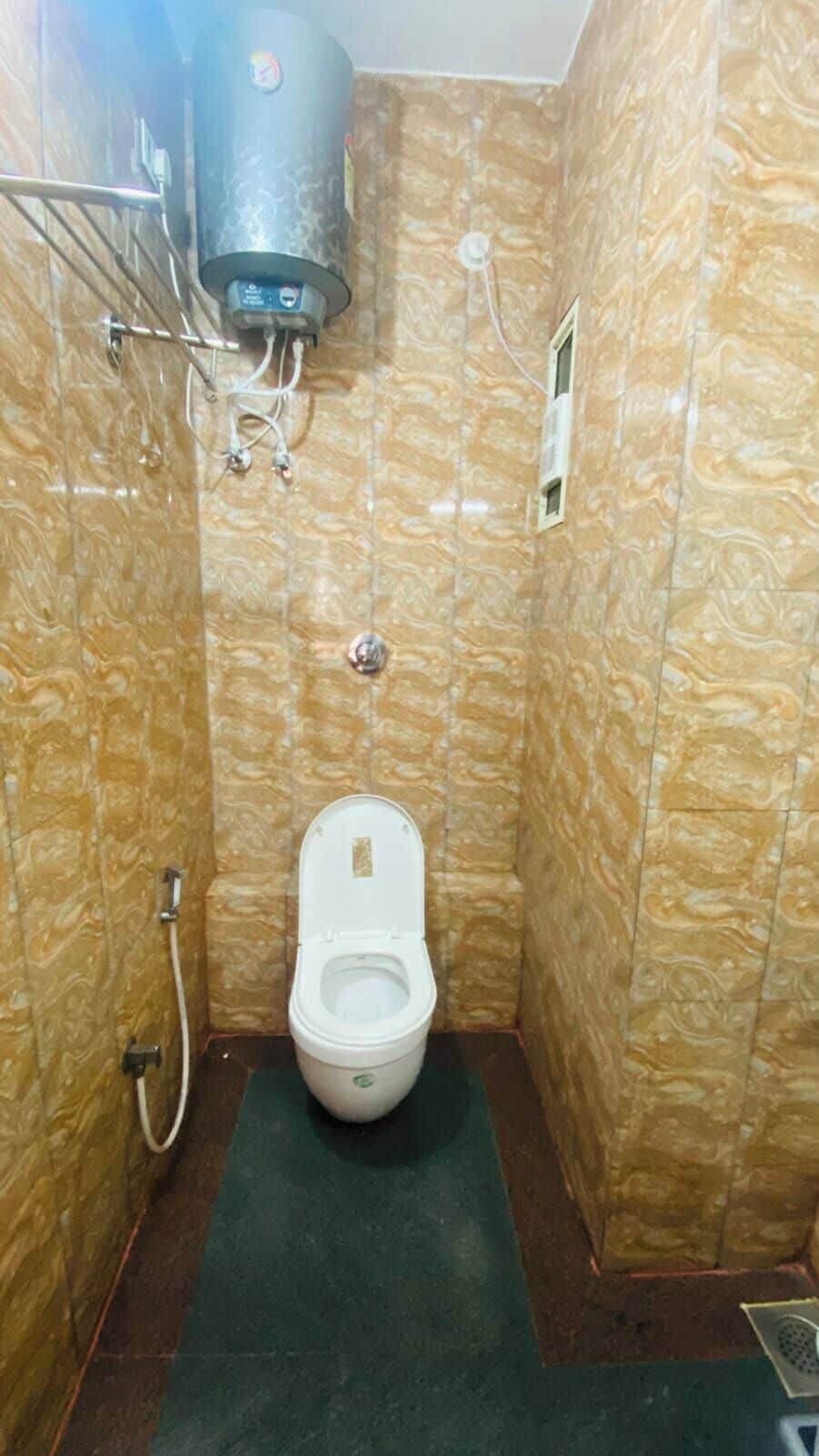 A bathroom with a marble-patterned wall, a toilet, a water heater, and a shower control panel.