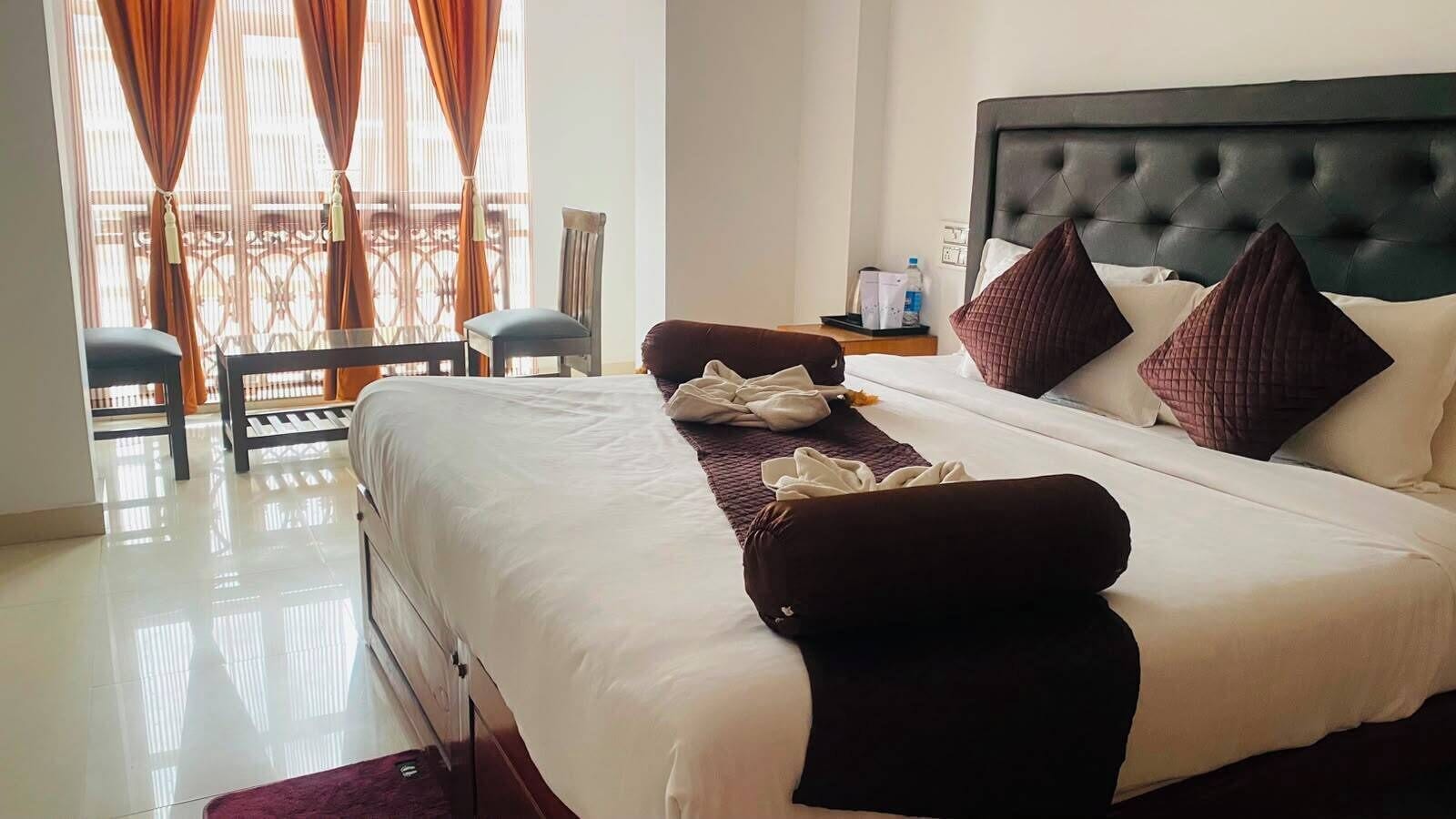 Une chambre d’hôtel avec un lit, une chaise, une table et une fenêtre avec des rideaux.