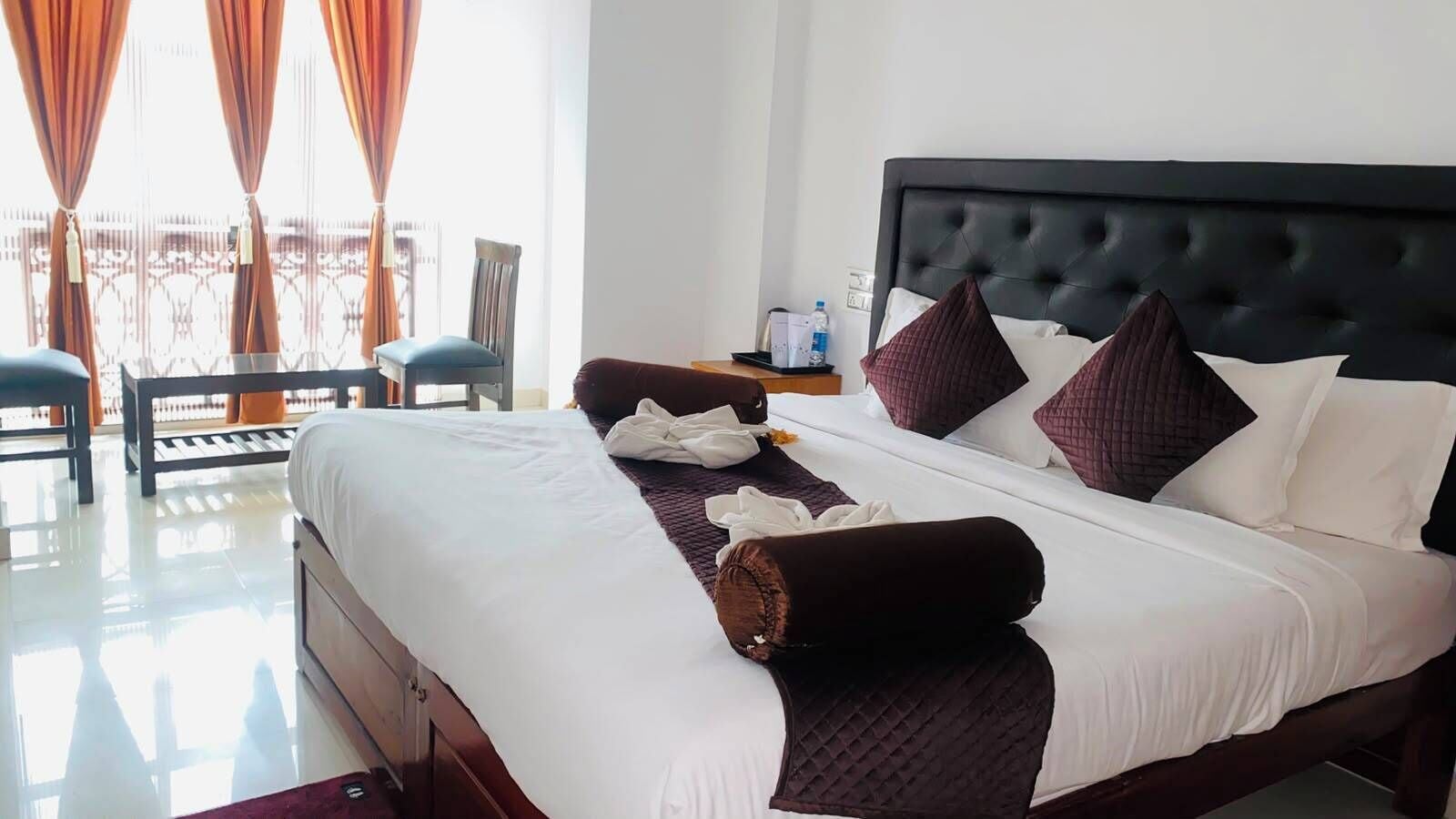 A hotel room with a large bed, a bedside table, a chair, and a view of the outdoors.