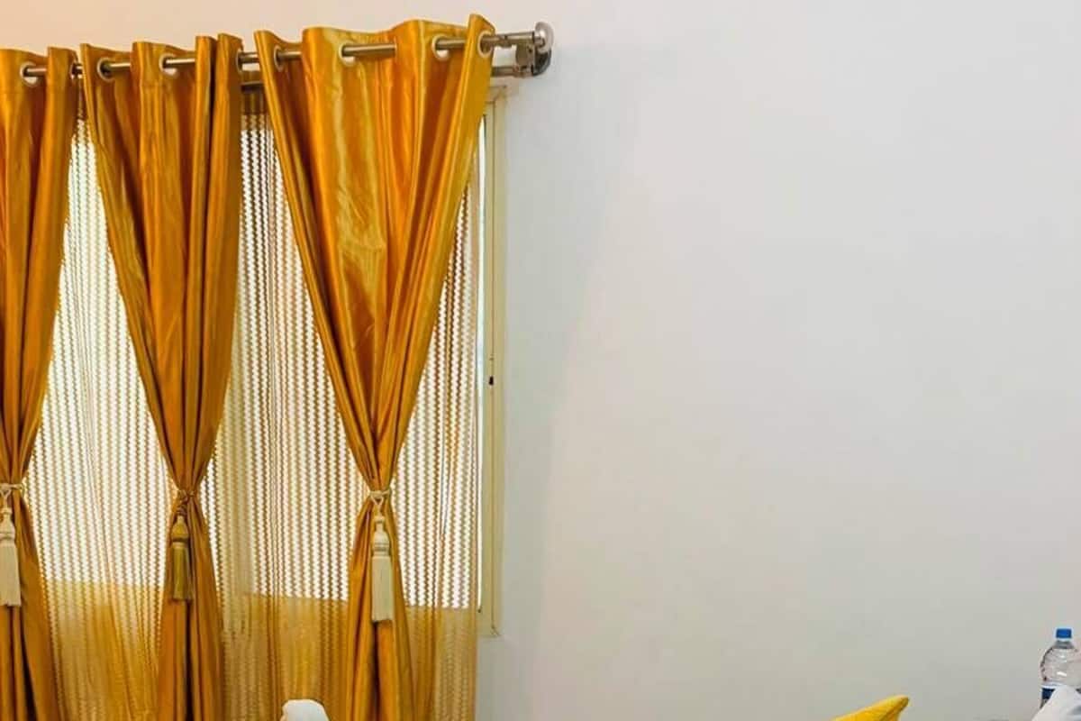 Een hotelkamer met een bed, gele kussens en een raam met gordijnen.