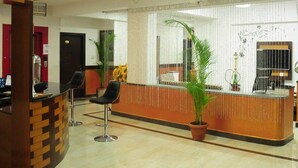 A reception area with a counter, two bar stools, a potted plant, and a decorative mirror. - Hotel Al Wesal International (Madikeri)