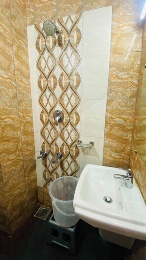 Un baño con ducha, lavamanos y un cubo de basura.