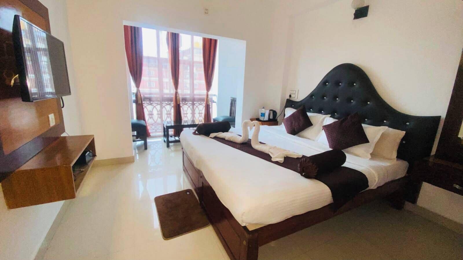 Een hotelkamer met een groot bed, een televisie, een balkon met gordijnen en uitzicht op de omgeving.