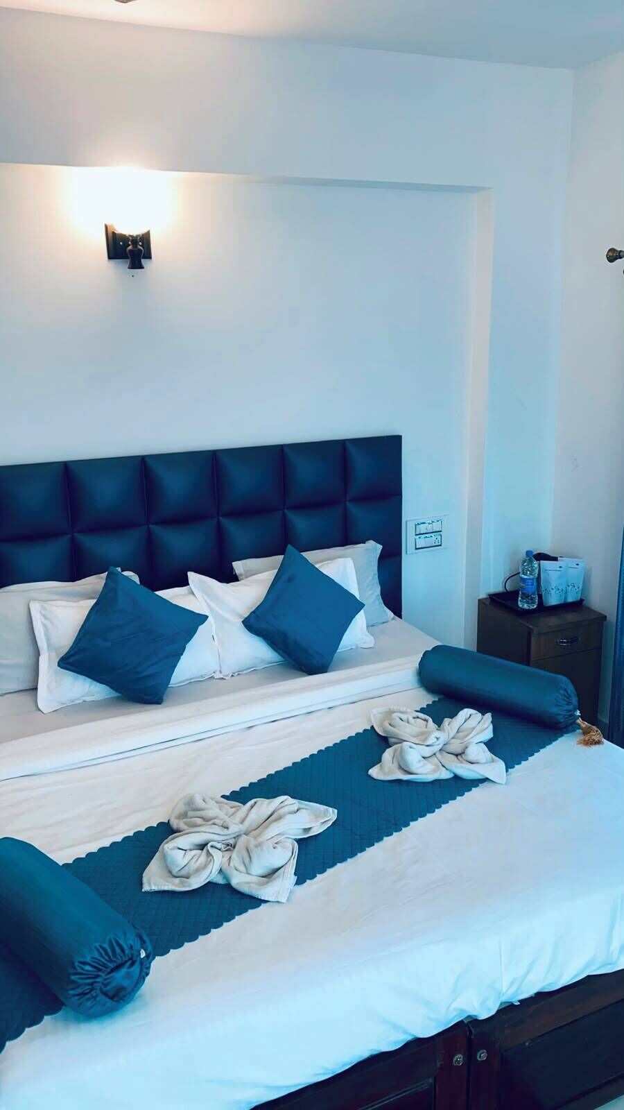 A neatly made bed with a dark headboard, white and blue pillows, and a blue bed runner.