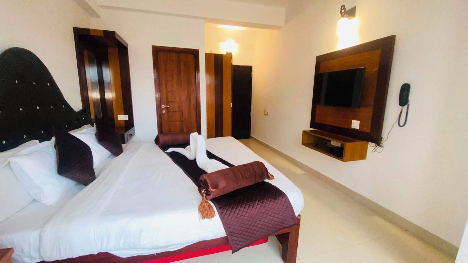 A hotel room with a large bed, a TV mounted on the wall, and a telephone.