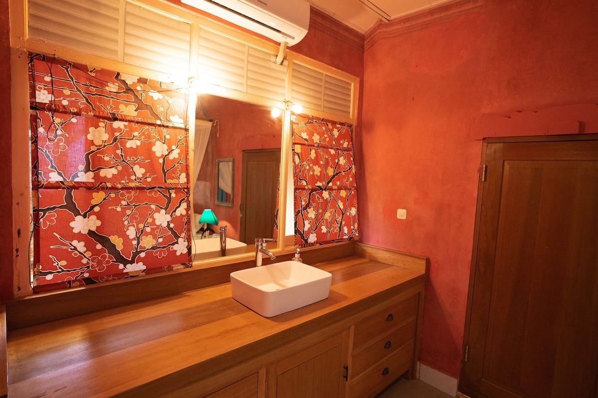A bathroom with a wooden vanity, a white sink, and a large mirror with floral wallpaper.