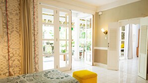 A room with a bed, a yellow ottoman, and a sliding glass door leading to a balcony with plants. - Sayan Ridge Villa (Ubud)