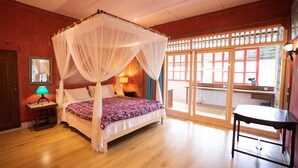 A room with a four-poster bed, a nightstand with a lamp, a wooden table, and a view of the outside through a glass door. - Sayan Ridge Villa (Ubud)