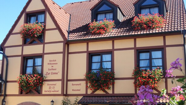 Un edificio tradicional con entramado de madera, con jardineras florales en las ventanas y un cartel dando la bienvenida a los huéspedes.
