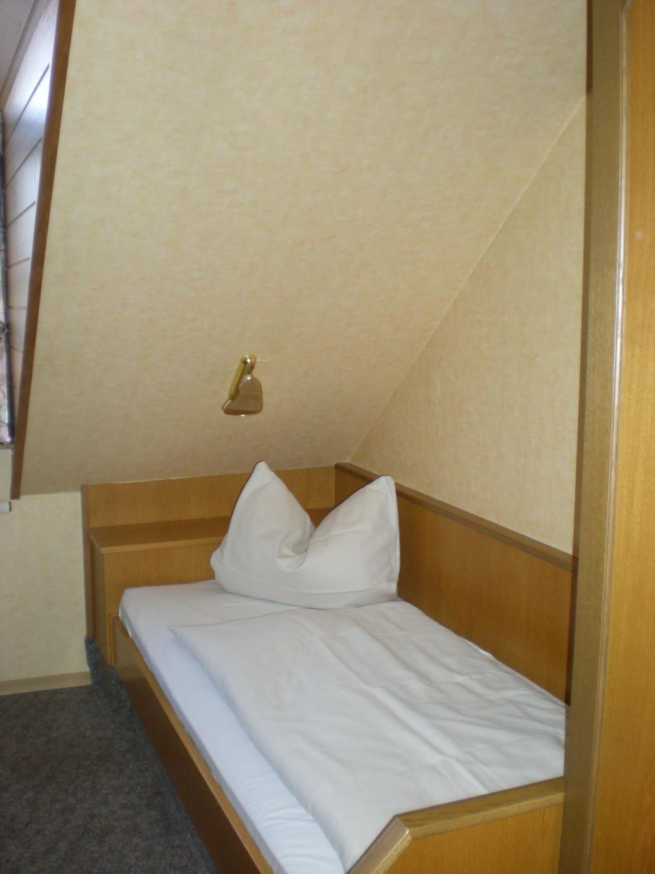 Ein Einzelbett mit einem Holz-Kopfteil in einem Raum mit schrägverdeckter Decke.