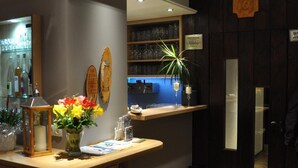 Zona de recepción de hotel con un mostrador de madera, una vitrina con botellas de vino, un jarrón con flores y un área de bar iluminada en azul al fondo.