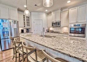 A kitchen with white cabinets, granite countertops, stainless steel appliances, and a bar area with stools.
