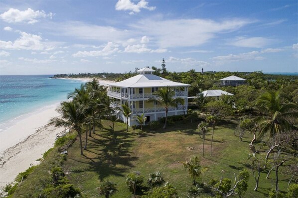 A coastal property with a large white building featuring multiple balconies, surrounded by palm trees and a beach.