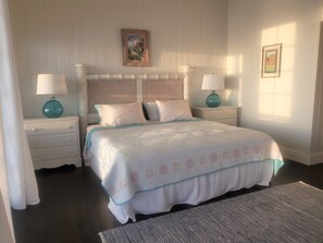 Une chambre à coucher bien rangée, avec un lit, deux tables de chevet dotées de lampes, un tableau encadré au mur et une fenêtre laissant entrer la lumière naturelle.