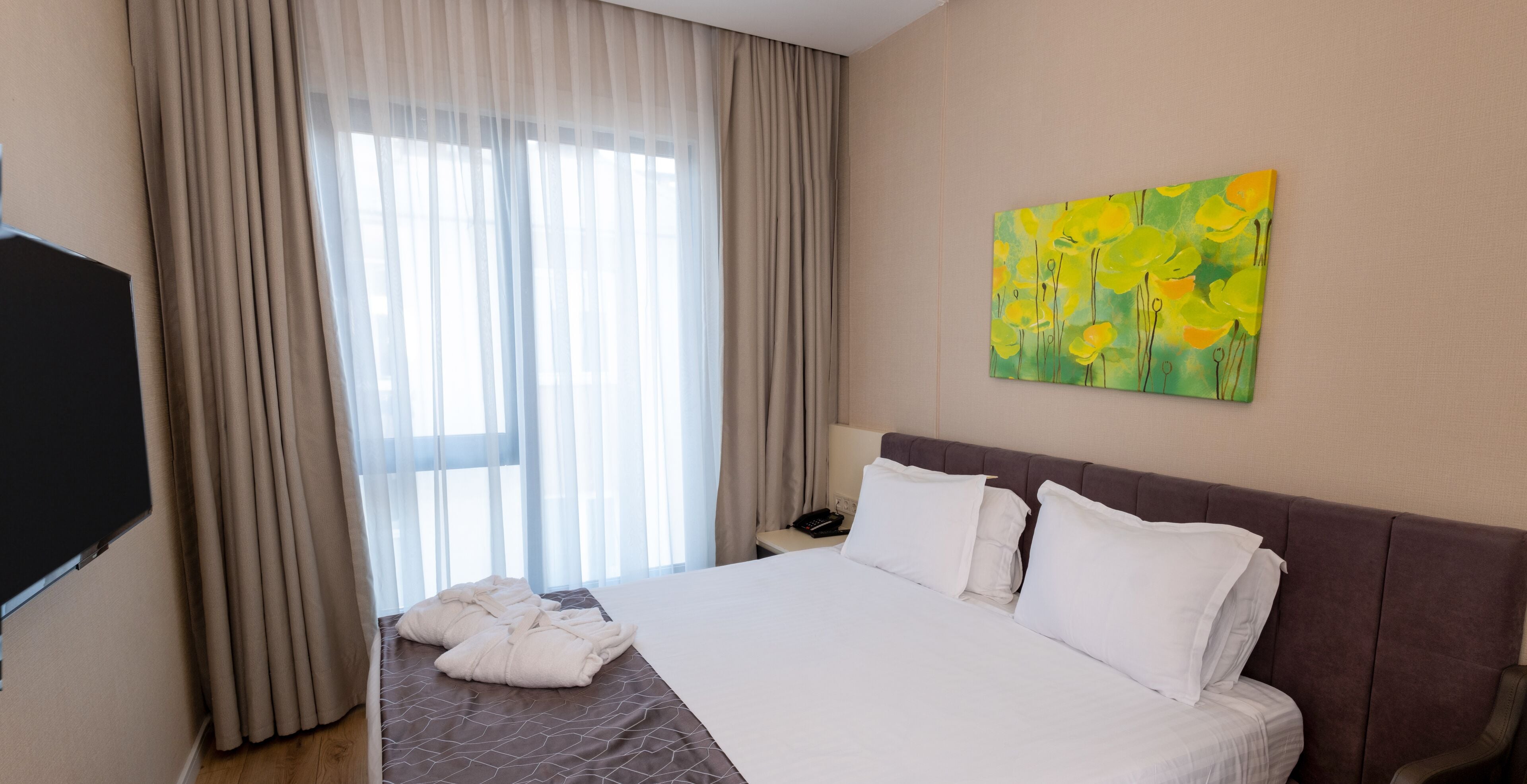 A hotel room with a bed, a painting, a TV, and curtains.