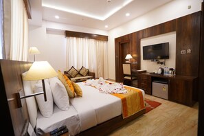 Quarto de hotel com cama, escrivaninha, televisão e mini-geladeira.
