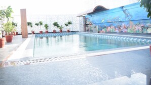 Una piscina con borde de baldosas, rodeada de plantas en macetas y un mural que representa un paisaje submarino.