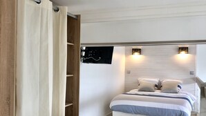 A bedroom with a bed, a wooden wardrobe, a TV mounted on the wall, and a ceiling light fixture. - Charming Duplex Trouville / Deauville 5mn Train Station (Trouville-sur-Mer)