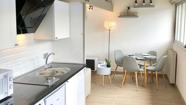 A compact kitchen with a washing machine, a dining area with a table and chairs, and a small seating area with a lamp. - Charming Duplex Trouville / Deauville 5mn Train Station (Trouville-sur-Mer)