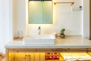 A bathroom with a white sink, a mirror, a wooden shelf with toiletries, a small potted plant, and a towel rack. - W Lodge (Qiandongnan)