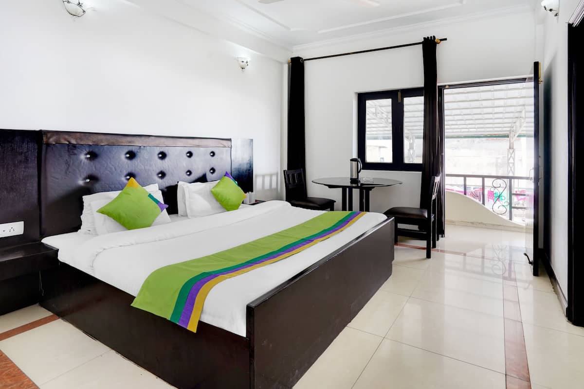 A hotel room with a large bed, a small table with a chair, and a window with a view of the outside.