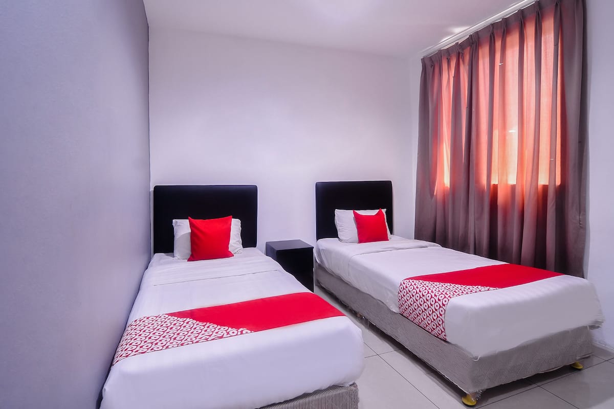 A hotel room with two single beds, each with a black headboard, white bedding, and red accents. The room has a modern design with a large window covered by curtains, allowing natural light to enter.