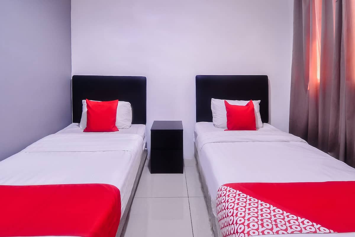 A hotel room with two single beds, each with a black headboard and red and white pillows. There is a small black nightstand between the beds.