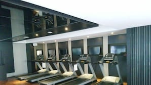 Ein Fitnessraum mit an einer Wand aufgestellten Laufbändern, Holzboden und modernem Design mit dunklen Wänden und Decke.