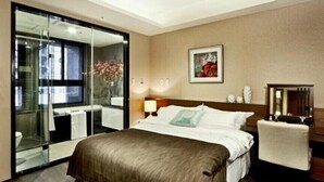 Ein Hotelzimmer mit einem großen Bett, einem Nachttisch, einem Sessel, einem Spiegel, einem Bild an der Wand und einer Schiebetür zum Badezimmer.
