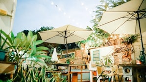 An outdoor patio area with tables and chairs under umbrellas, surrounded by potted plants and a brick wall. - No. 79 Backpacker (Kaohsiung)