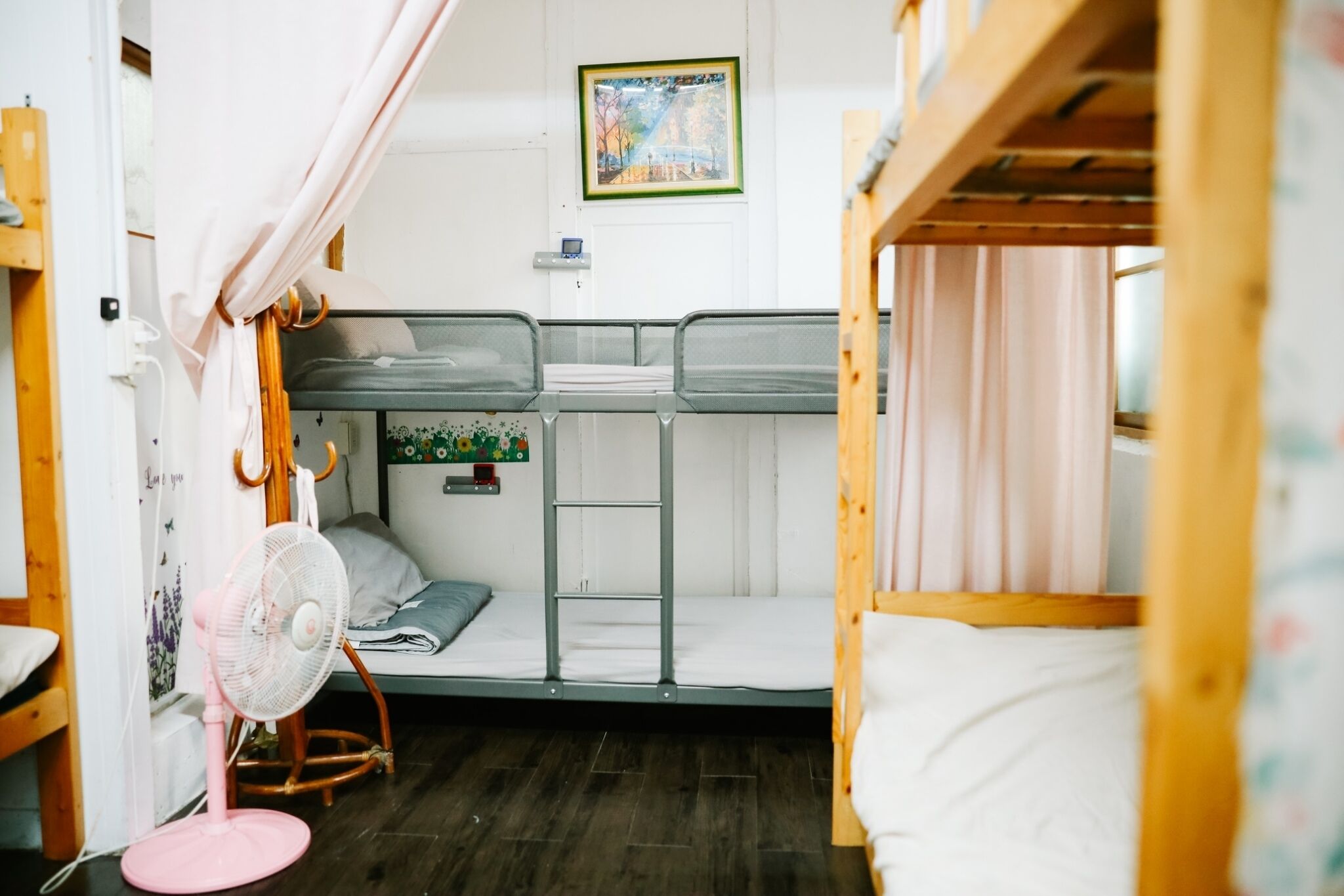 Un dormitorio con literas, un ventilador, un estante pequeño con una planta y una puerta con cortina.