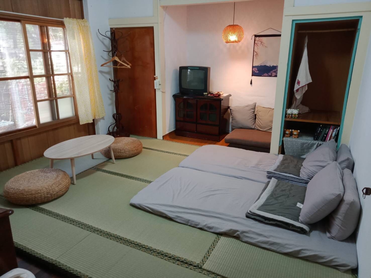 A traditional Japanese-style room with tatami flooring, a low table, a sofa, a television, and a wardrobe.
