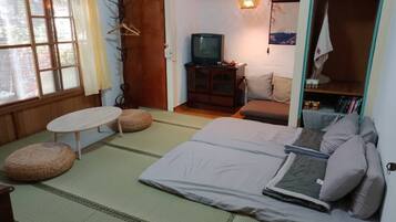 A traditional Japanese-style room with tatami flooring, a low table, a sofa, a television, and a wardrobe.