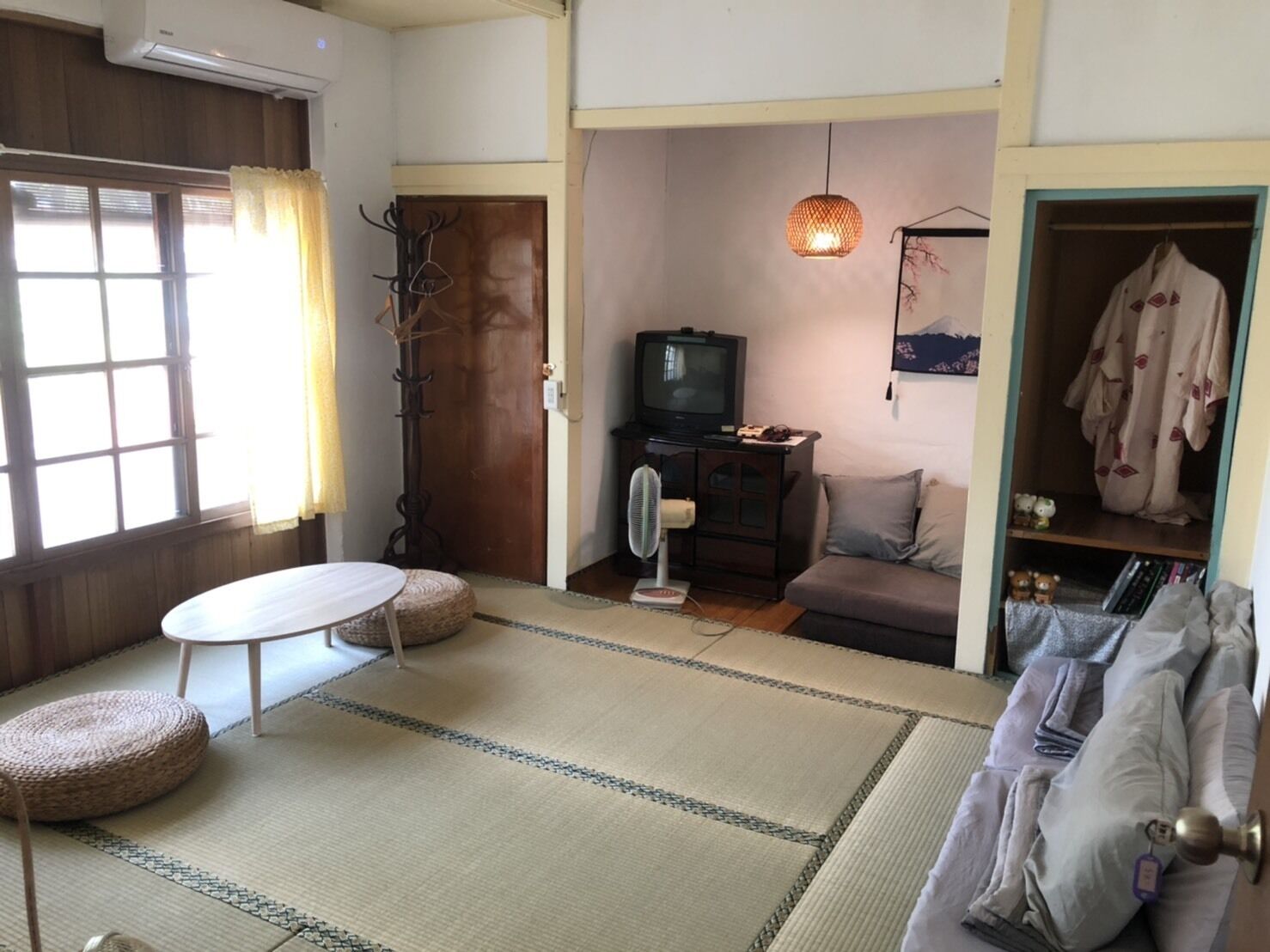 A traditional Japanese-style living room with tatami flooring, a low table, a sofa, a television, and a wardrobe.