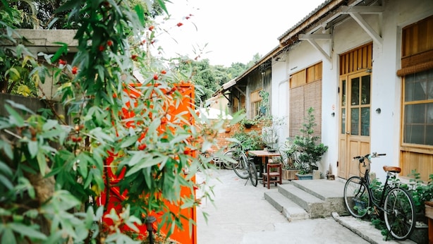 A narrow alleyway with a building on the right, a bicycle, and a table with chairs. - No. 79 Backpacker (Kaohsiung)