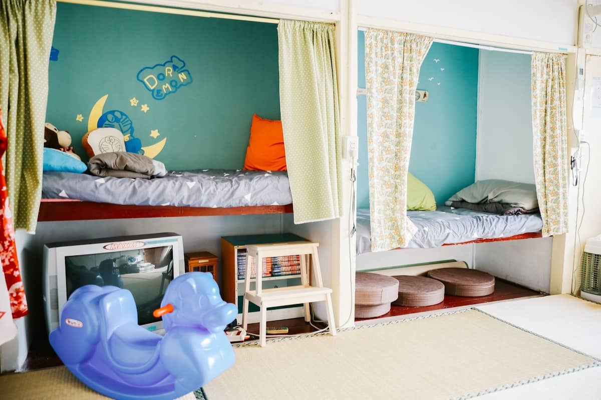 Quarto infantil com beliches, uma TV pequena, um brinquedo e uma estante de livros.
