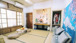 A room with tatami flooring, a low table with a yellow plush toy, a sofa with cushions, and a wardrobe with clothes. - No. 79 Backpacker (Kaohsiung)