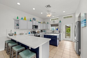 A modern kitchen with white cabinets, a central island with stools, and a refrigerator.