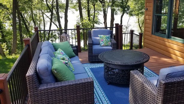 Een terras met rieten meubels, een ronde tafel en uitzicht op een meer.