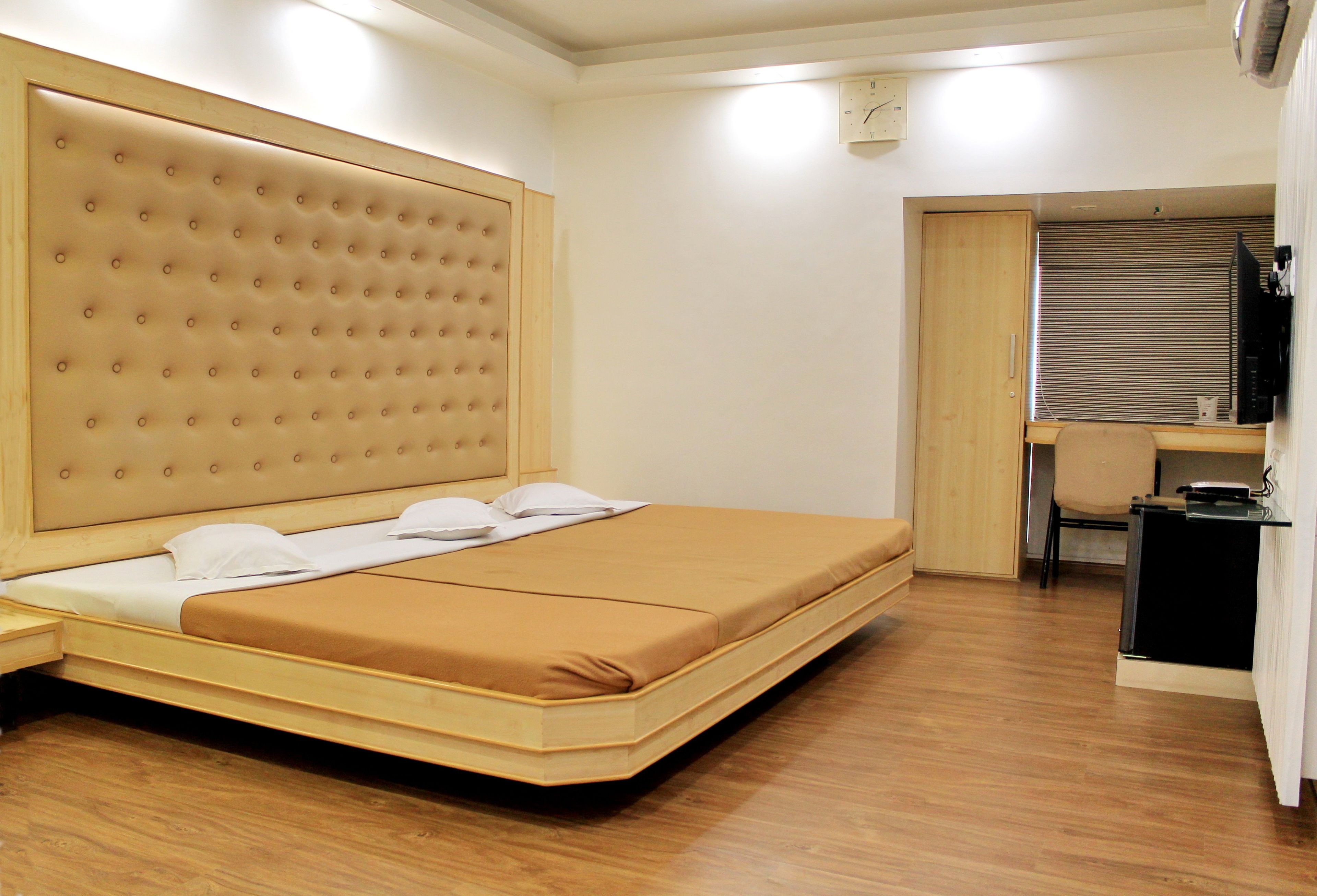 Ein Schlafzimmer mit einem großen Bett, einem hölzernen Kopfende, einem kleinen Schreibtisch und einem Fenster mit Jalousien.