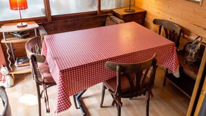 A room with a checkered table, chairs, a lamp, a window with a view, and a wooden wall.