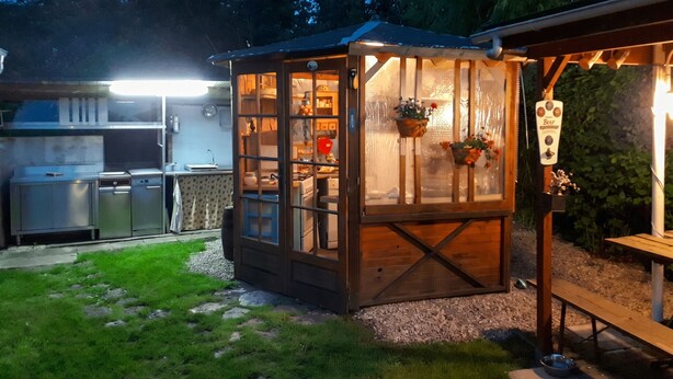 A wooden structure with a glass door, a grill area, and a wooden table with a bench.