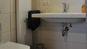 A bathroom with a toilet, sink, mirror, and a trash bin. - Gästehaus Sonne (Triefenstein)